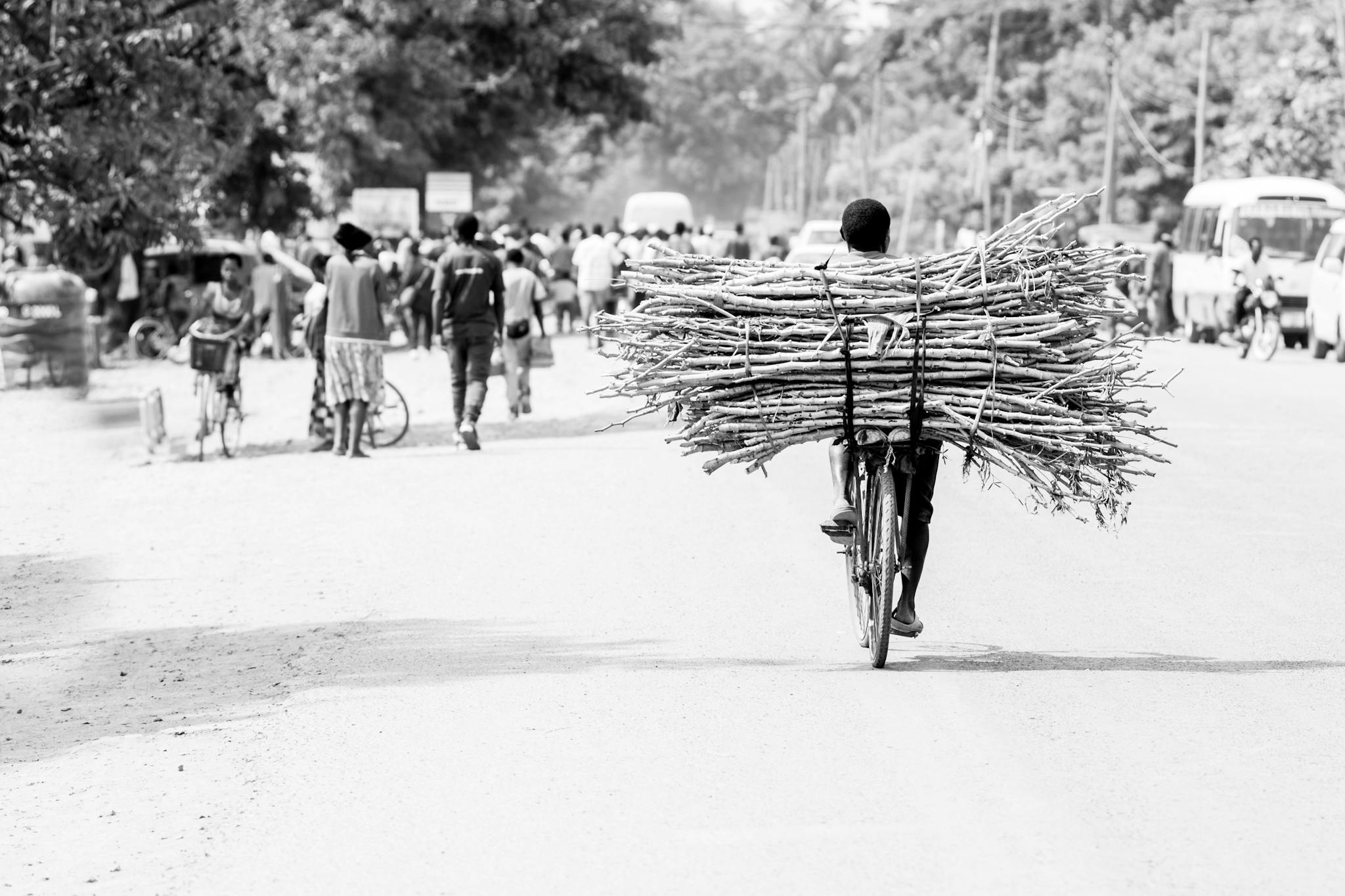 A person transports firewood on a bicycle down a busy street in Kyela, Tanzania.