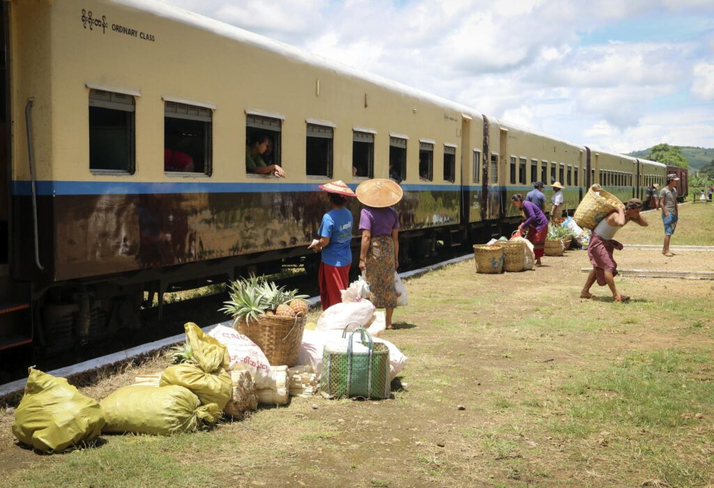 Vendors and villagers exchange goods near a train in Hsipaw, showcasing Myanmar's rural market life.