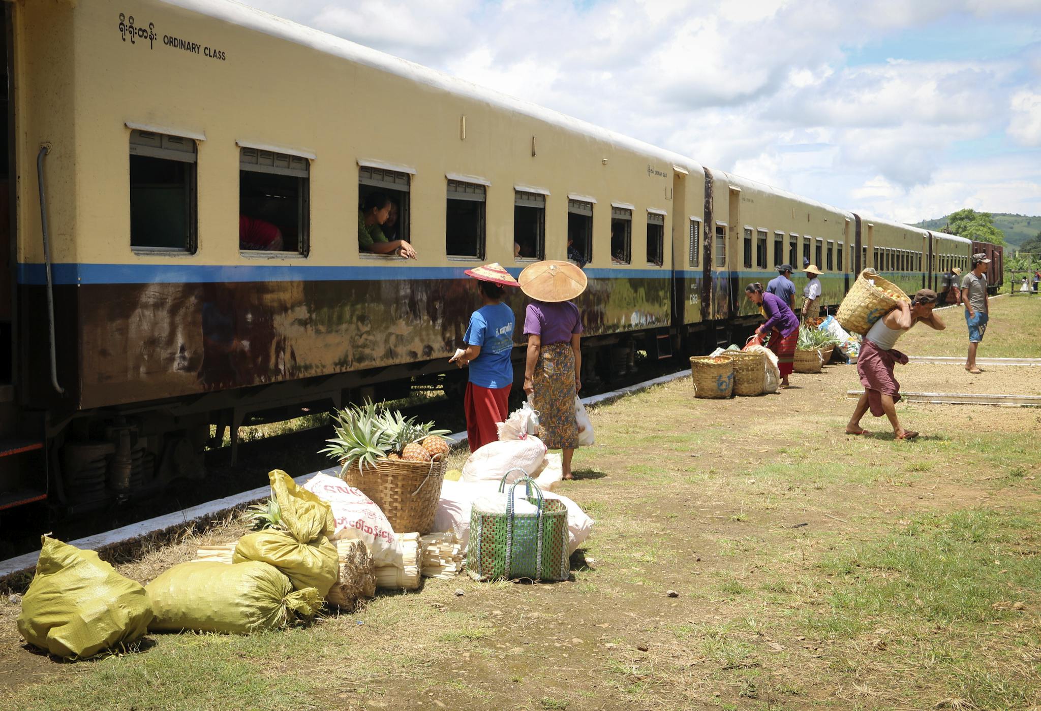 Vendors and villagers exchange goods near a train in Hsipaw, showcasing Myanmar's rural market life.